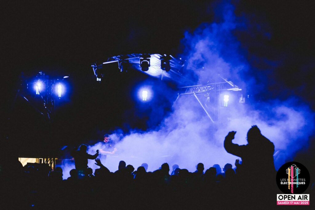 Plan large depuis l'arrière de la foule la nuit, regardant la scène principale du festival Les Bonnettes Électroniques.